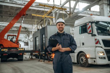 Ön manzara, elinde not defteri, ayakta. Erkek işçi, modern depo veya imalat şirketinde çalışıyor..