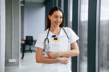 Not defterini elinde tutuyor. Beyaz önlüklü kadın doktor içeride..