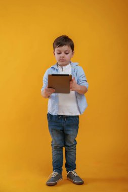 Tablet ellerde. Küçük çocuk sarı arka planda stüdyoda..