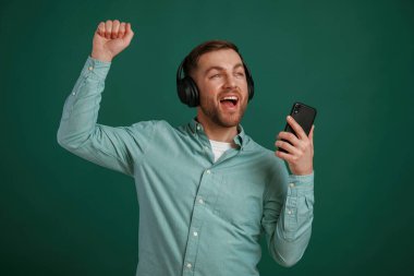 Gülümsüyor, müzikten zevk alıyor. Adam stüdyoda arka planda duruyor..