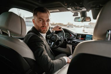 Kameraya bakıyorum. Siyah takım elbiseli adam arabada oturuyor..