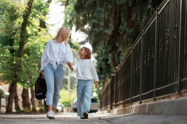 Kızını okula götürüyor. Annesiyle birlikte küçük bir kız dışarıda..