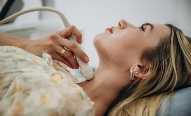 Kadın uzanıyor ve tiroid bezinin ultrasonik testinden geçiyor..