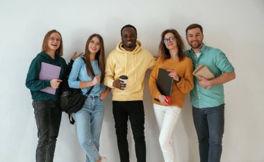 Not defterleri ve kahve fincanı tutuyor. Bir grup genç beyaz arka planda duruyor..