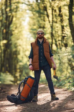 Sarı balta elinde, sırt çantası yerde. Sakallı adam gündüz vakti ormandadır..