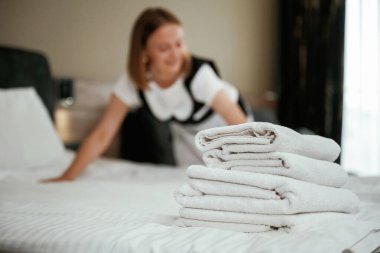 Yatağın üzerinde bir sürü yeni bez var. Genç oda hizmetçisi otel odasında..