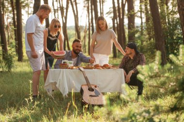 Olumlu ruh hali, eğlenmek. Bir grup arkadaş, ekolojik kutularda yiyeceklerle sahada piknik yapıyorlar..