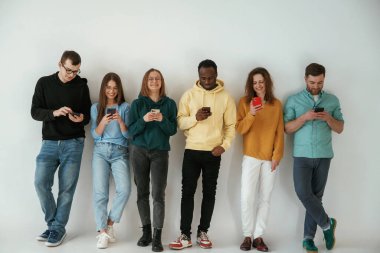 Neşeli, elinde akıllı telefonlar. Bir grup genç beyaz arka planda duruyor..