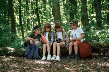 Dinleniyor, kamera ve su şişesini tutuyor. Çocuklar yazın gündüz vakti ormanda..