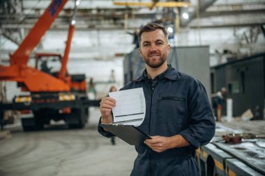 Ön manzara, elinde not defteri, ayakta. Erkek işçi, modern depo veya imalat şirketinde çalışıyor..