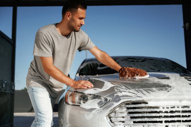 Otomobili yıkamaya odaklanmış. Adam dışarıda arabasıyla bekliyor..