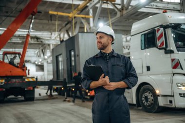 Ön manzara, elinde not defteri, ayakta. Erkek işçi, modern depo veya imalat şirketinde çalışıyor..
