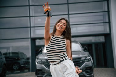 Anahtarları olan yeni arabanın mutlu sahibi. Çekici genç bayan dışarıda, yepyeni arabasının yanında..