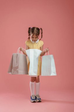 Alışveriş torbalarıyla. Şirin küçük kız pembe arka plana karşı..
