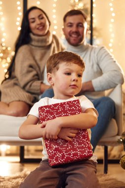 Kırmızı hediye kutusu olan bir çocuk. Mutlu bir aile yeni yılı evde kutluyor..