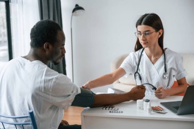 Masanın başında oturuyor. Kadın doktor bir erkeğin kan basıncını ölçer..