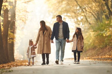 Sonbahar parkı. Anne, baba ve iki kızın mutlu aileleri ormanda, yolda.