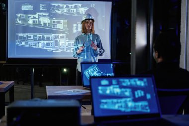 Kadın mimar projektör üzerine inşaat alanı planı gösteriyor.