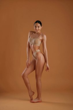 Arkasında turuncu renkli duvar var. İnce vücutlu kadın arka planda poz veriyor..