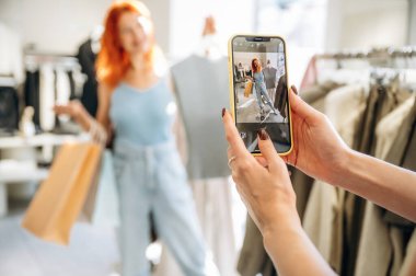 Akıllı telefon kullanarak fotoğraf çekmek. İki bayan arkadaş perakende mağazasında kıyafet seçiyorlar, alışveriş yapıyorlar..