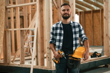 Evi inşa ediyor, elinde şapka ve matkapla. Ahşap depoda sanayi işçisi..