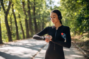 Saate, saate, izleyiciye bakıyorum. Genç, sıska kadın dışarıda siyah spor kıyafetleri giyiyor..