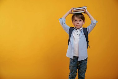 Kitapla oynamak, onu kafasında tutmak. Küçük çocuk sarı arka planda stüdyoda..
