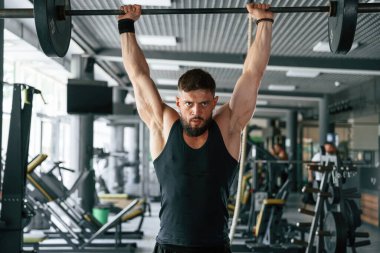 Halter kaldırıyor. Güçlü kaslı adam spor salonunda çalışıyor..