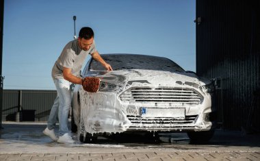 Yüzeyi temizliyor, araba yıkıyor, adam dışarıda arabasıyla bekliyor..