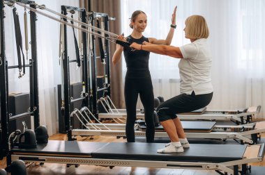 Eğitim ekipmanlarını kullanarak. Kadın eğitmen yaşlı kadının egzersiz yapmasına yardım ediyor..