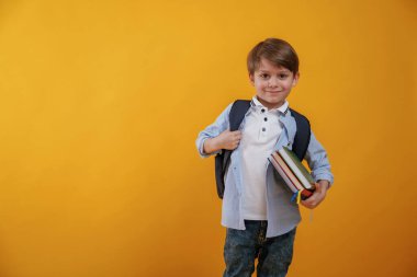 Okul için hazır, elinde kitaplarla. Küçük çocuk sarı arka planda stüdyoda..