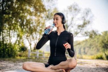 Kırsal alanda. İçme suyu. Oturuyorum. Genç, sıska kadın dışarıda siyah spor kıyafetleri giyiyor..