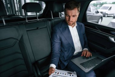 Çalışıyor, dizüstü bilgisayar kullanıyor. İşadamı yeni arabasında..