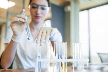 Test tüplerinde sıvı kullanarak kimyasal araştırma. Beyaz önlüklü kadın doktor içeride..