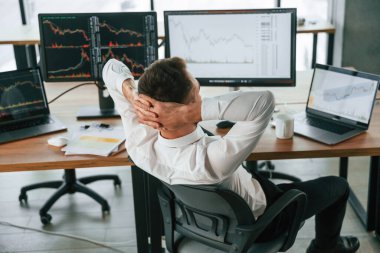 Ellerin başının arkasında oturuyorsun. İşadamı bilgisayar başında ve ofiste çalışıyor..