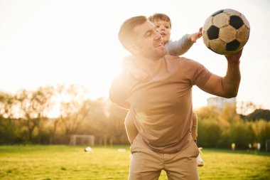 Omuzlarında, futbol topuyla. Mutlu baba ve oğul yazın sahada eğleniyorlar..