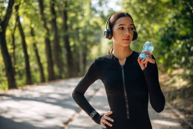 Şişede taze su var. Genç, sıska kadın dışarıda siyah spor kıyafetleri giyiyor..