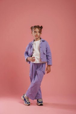 Durup poz vermek. Şirin küçük kız pembe arka plana karşı..