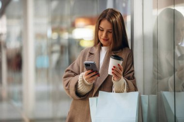 Bir fincan kahve ve telefon ellerde. Alışveriş merkezinde güzel bir kadın var, alışveriş anlayışı..