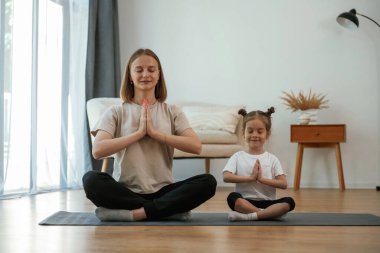 Sakin, nilüfer pozisyonunda. Küçük kızı olan genç bir kadın evde yoga yapıyor..