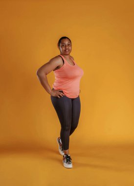 Spor kıyafetleri içinde. Afrikalı Amerikalı kadın sarı arka planda stüdyoda..