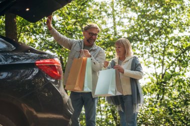 Bagaj açık, alışveriş torbaları var. Doğada üst düzey çiftler birlikte..
