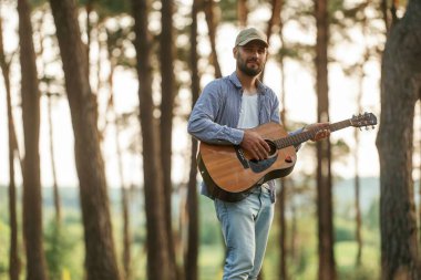 Yakışıklı adam akustik gitarla ormanda..