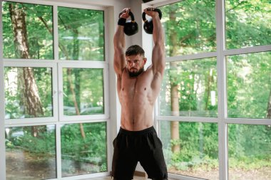 Pencerelere yaslanın. Dambıllı. Güçlü kaslı adam spor salonunda çalışıyor..