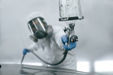 Koruyucu maskeyle ve giyerek. Spreyciyle araba boyayan adamın yakın görüntüsü..