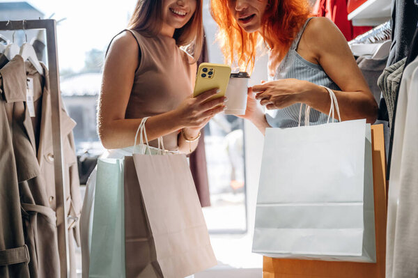 Some information in smartphone, reading. Two female friends are in the retail store, choosing clothes, shopping.