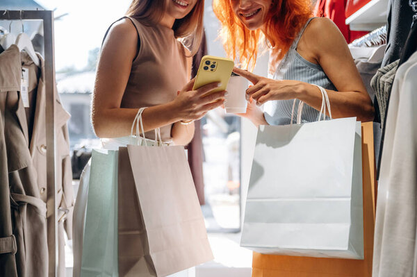 Some information in smartphone, reading. Two female friends are in the retail store, choosing clothes, shopping.
