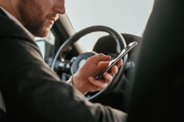 Akıllı telefon kullanarak internette sörf yapmak. Siyah takım elbiseli adam arabada oturuyor..