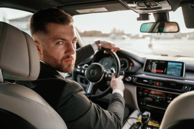 Kameraya bakıyorum. Siyah takım elbiseli adam arabada oturuyor..