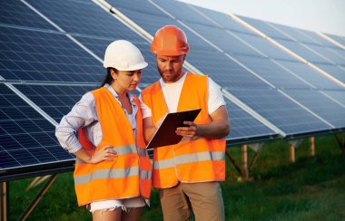 Not defterindeki bilgileri okuyorum. Kadın ve erkek, işçiler güneş panellerinin yakınındalar, üniformalılar..